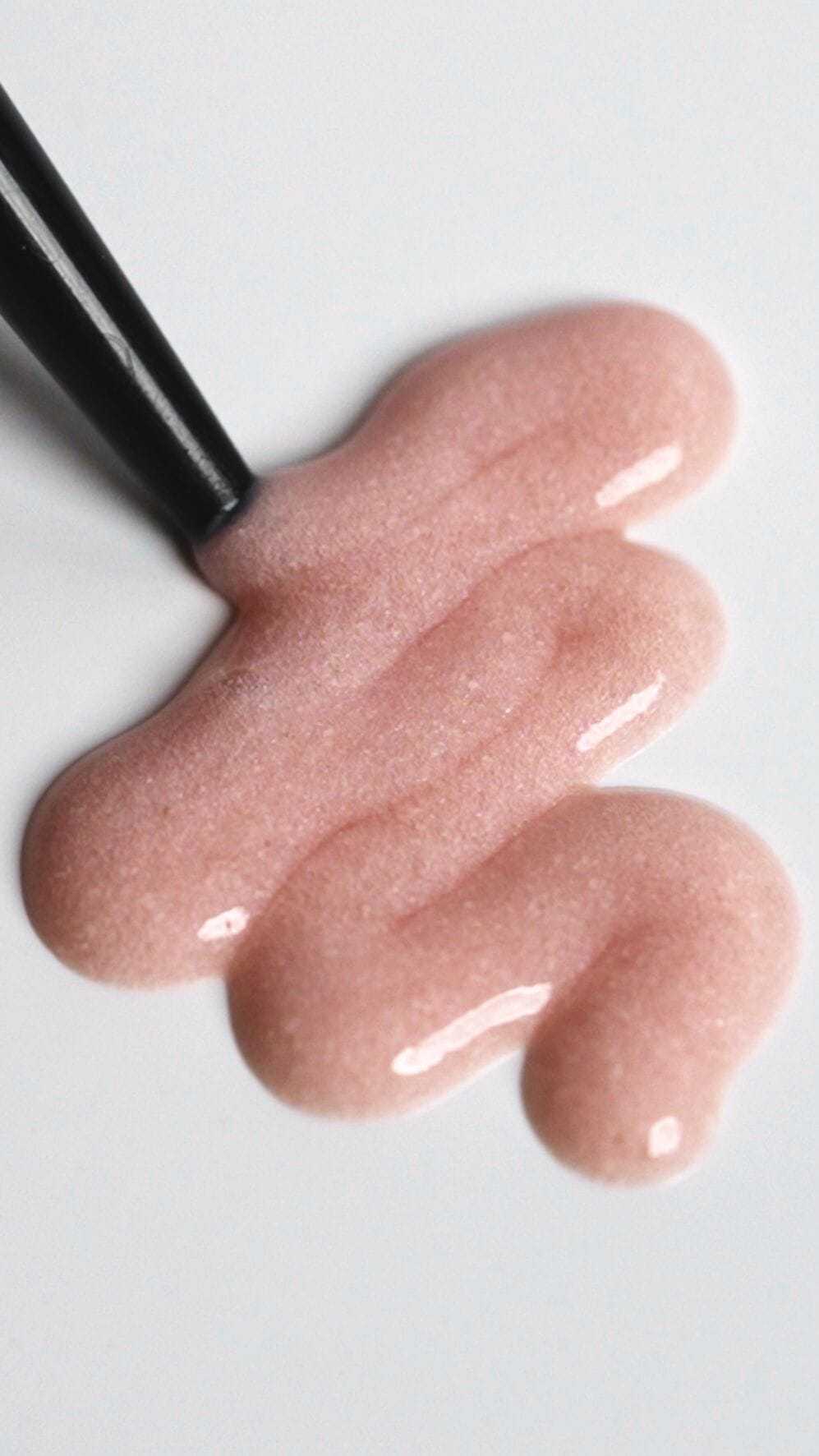 Shimmering pink nail polish with a brush against a white background.