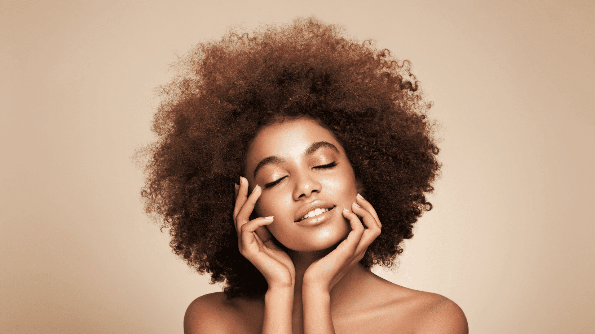 Woman with eyes closed, hands touching face, having curly hair against a beige background.
