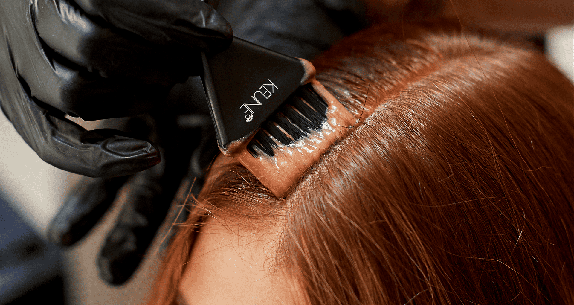 Hair dye being applied to a person's roots with a brush.