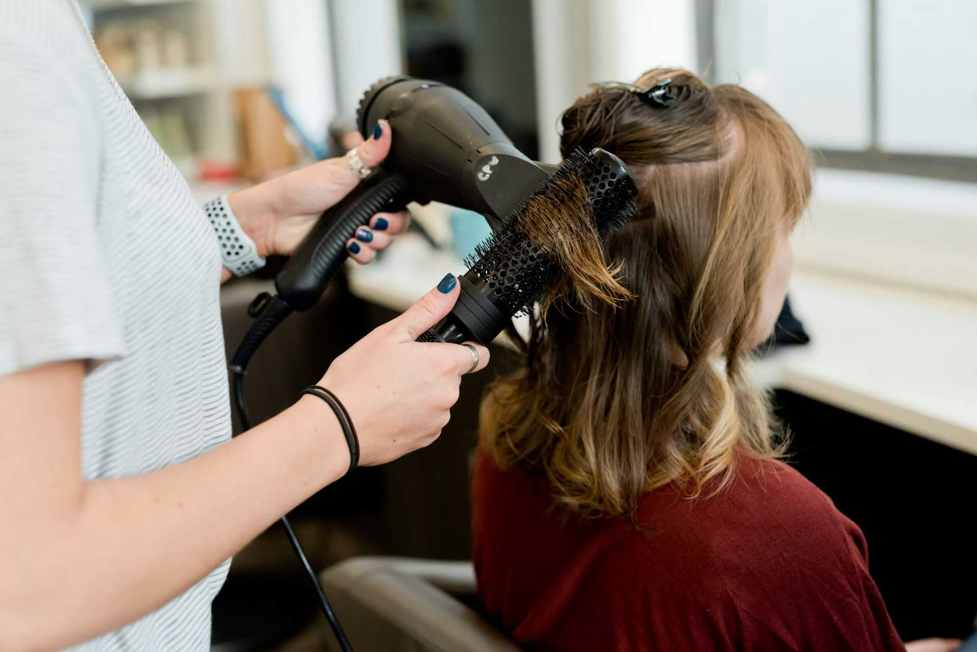 Hairstylist blow-drying a client's hair with a round brush in a salon.