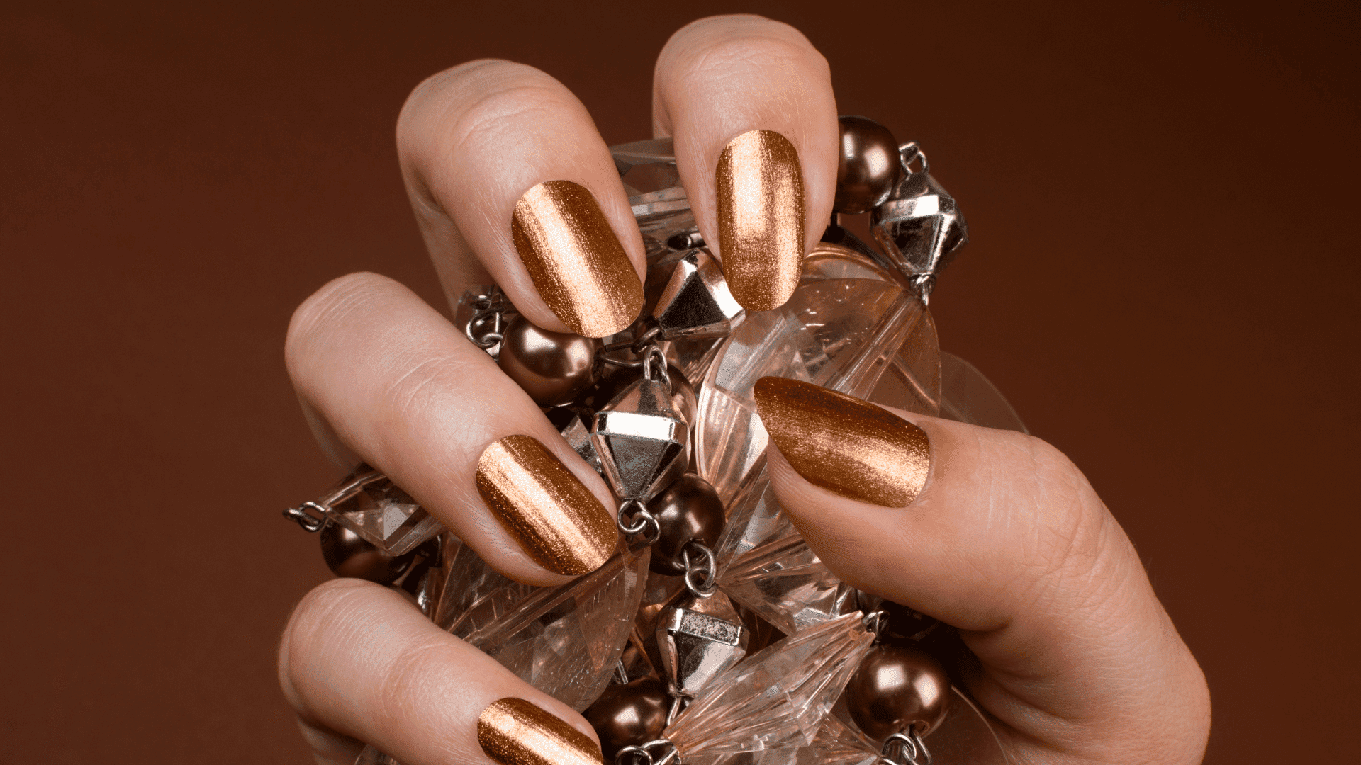 Shiny bronze manicured nails holding a crystal-accented bracelet.
