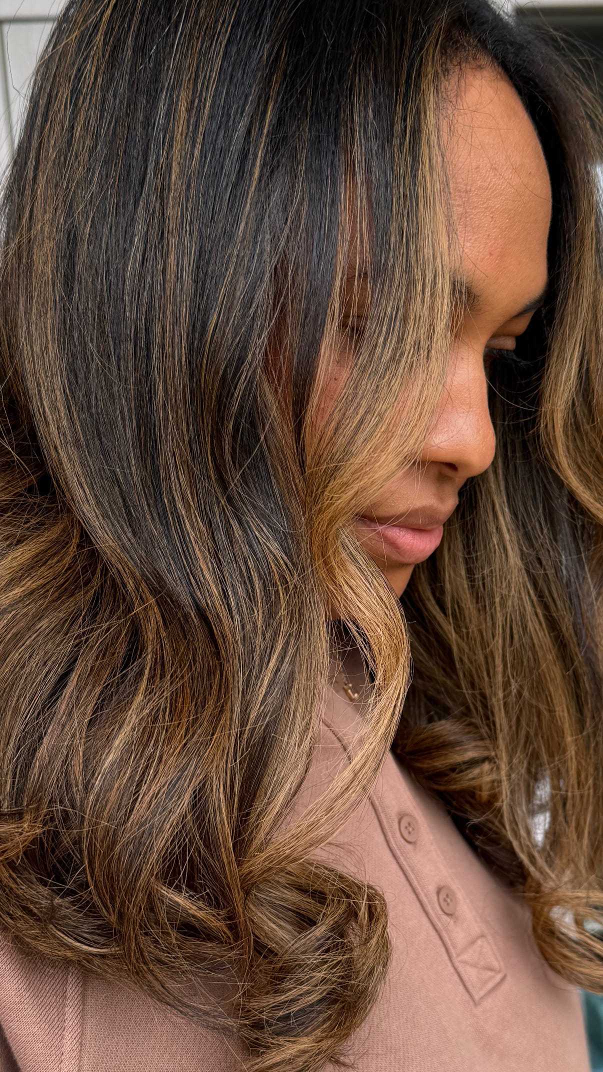 Woman with long wavy hair looking down, wearing a brown shirt.